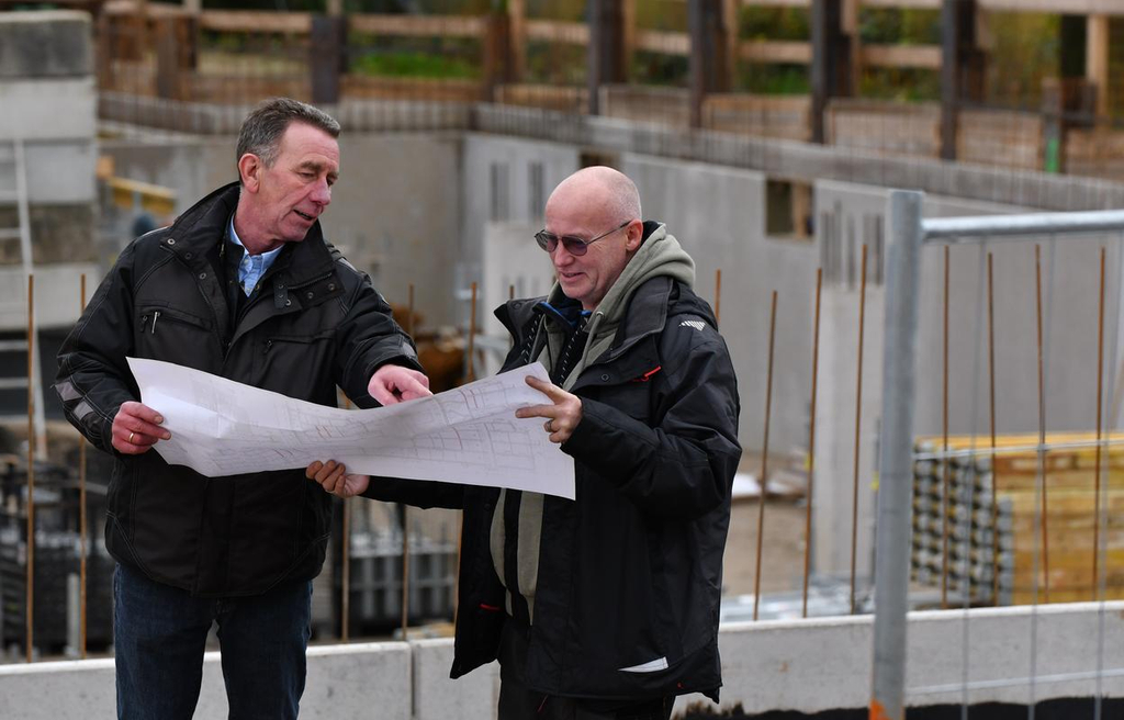 Zwei Männer stehen auf einer Baustelle und schauen sich gemeinsam einen Plan an. 