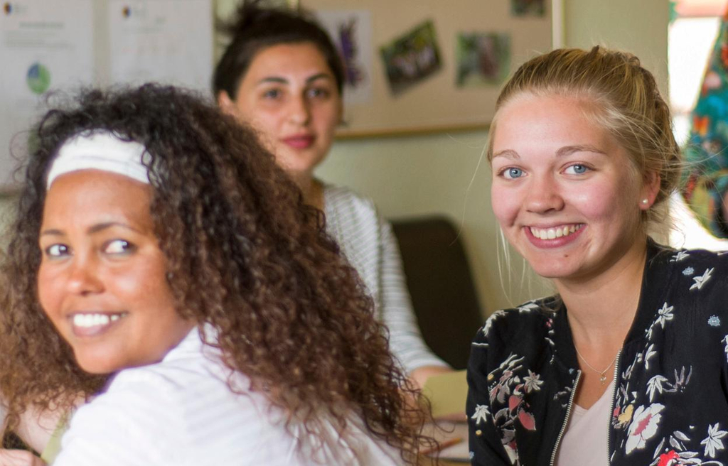Eine Gruppe Frauen sitzt an einem langen Tisch. Zwei der Frauen haben sich zur Kamera gedreht und lächeln. 