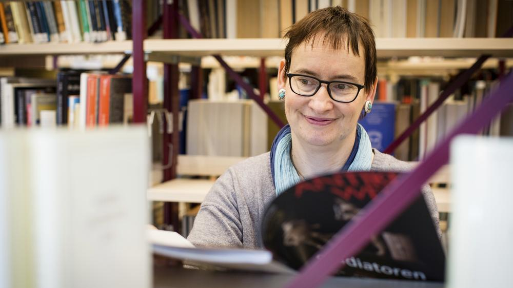 Agnes steht vor einem Bücherregal und liest eine Zeitschrift.