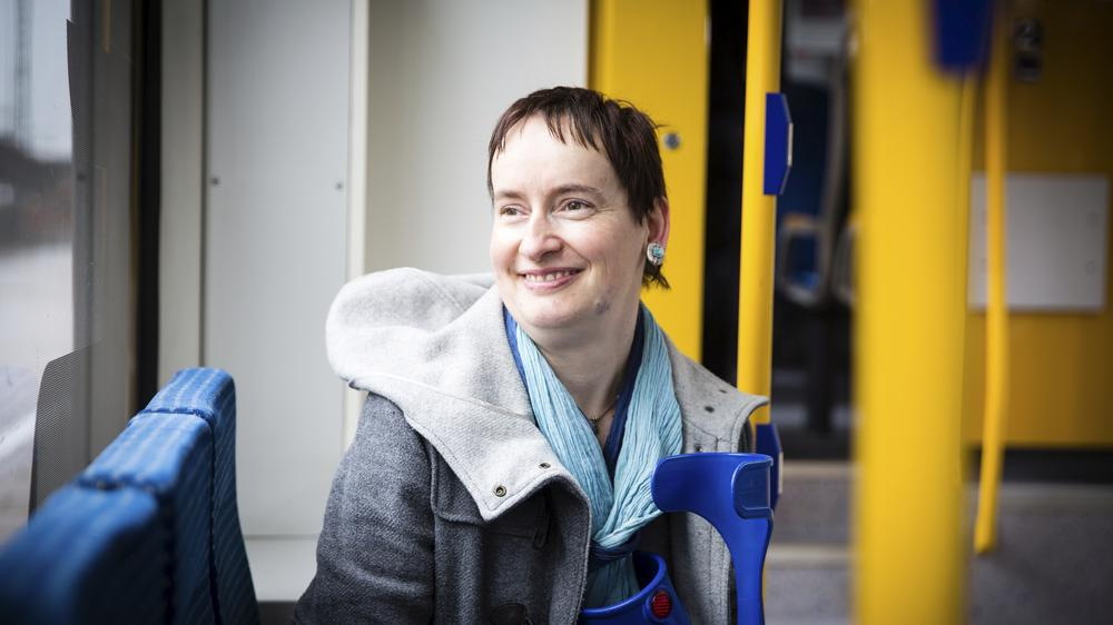 Agnes sitzt im Zug, lächelt und schaut aus dem Fenster.