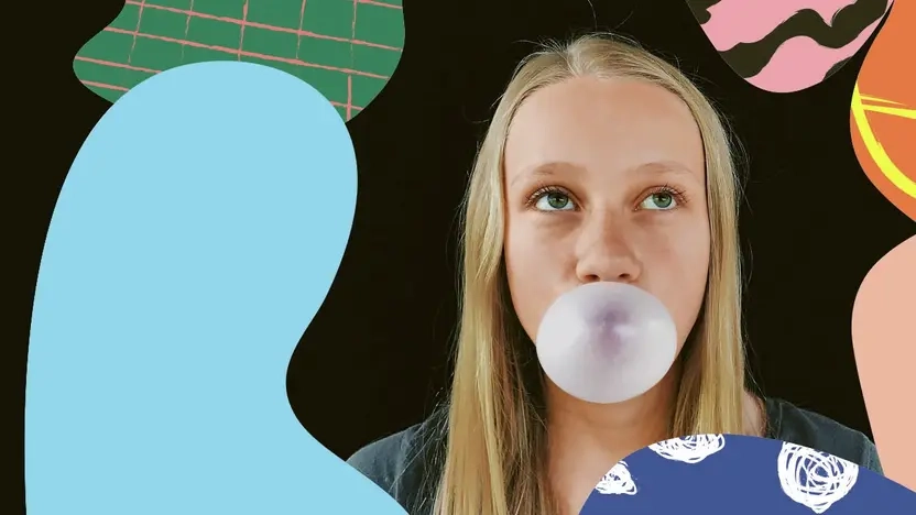 Ein Mädchen mit langen blonden Haaren macht eine Kaugummiblase.