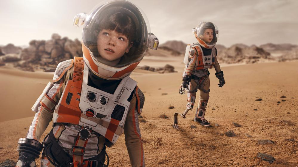 Zwei Kinder in Raumanzügen laufen über die Oberfläche des Mars. Eines der Kinder hat eine Beinprothese.