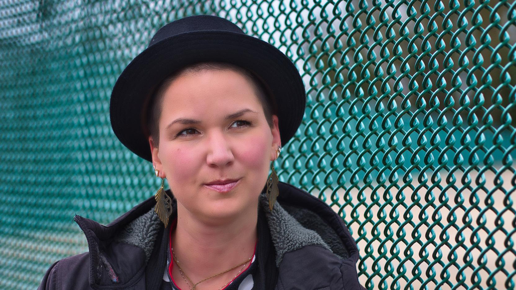 Eine Frau mit einem schwarzen Hut steht vor einem Zaun