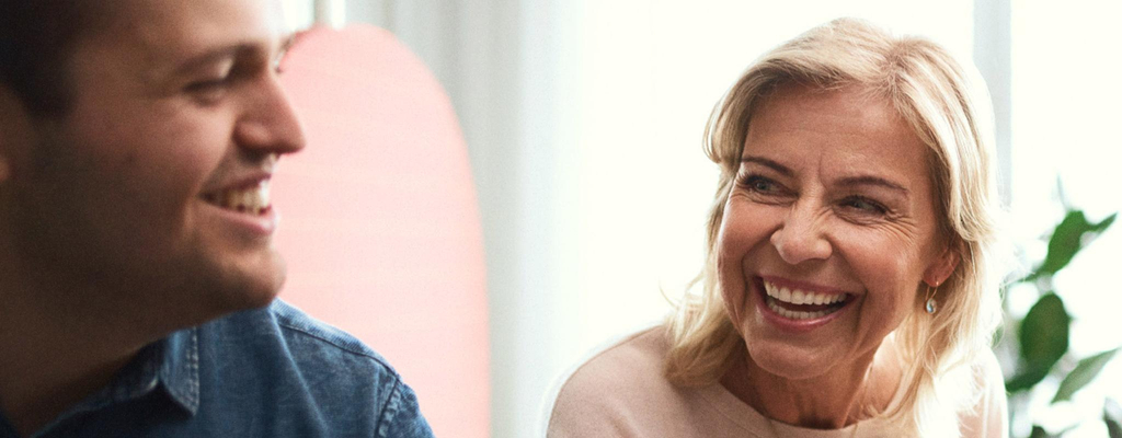 Ein junger Mann und eine blonde Frau sitzen gemeinsam vor einem Computerbildschirm. Die beinen lachen sich freundlich an.