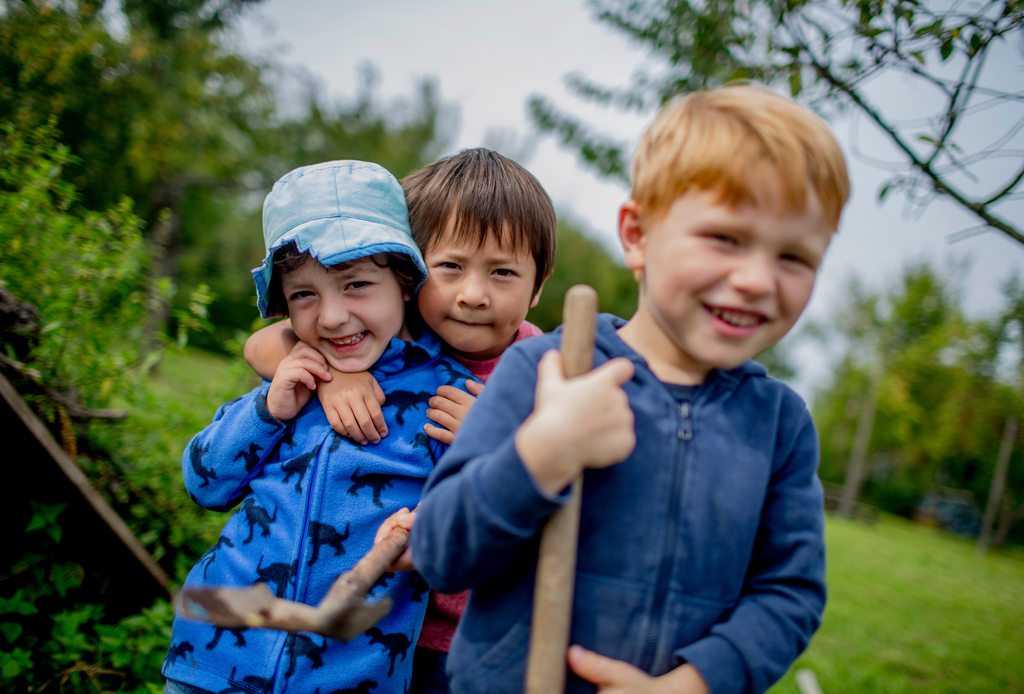 Drei Kinder in der Natur lachen in die Kamera.