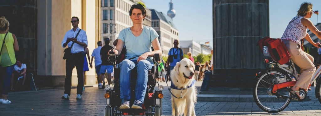 Eine Frau im Rollstuhl mit Hund in einer Straßenszene in Berlin