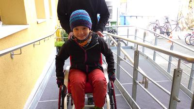 ein kind im rollstuhl wird eine rampe hochgeschoben