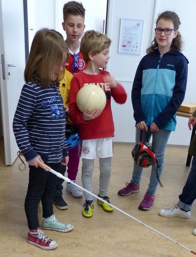 eine gruppe von kindern, ein mädchen hält einen blindenstock in der hand