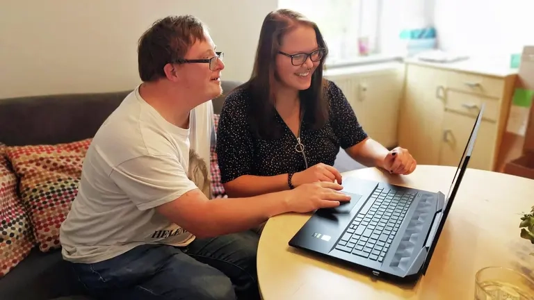 Ein Mann mit Downsyndrom und eine Frau vor einem Laptop