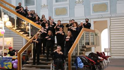 Die Mitglieder des Gebärdenchores stehen auf einer Treppe und lachen in die Kamera.