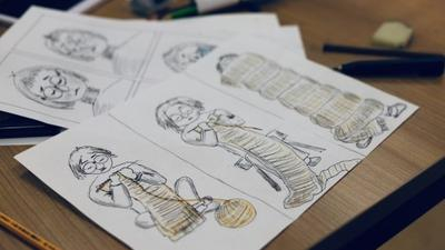 Mehere Blätter mit Comiczeichnungen liegen auf einem Holztisch.