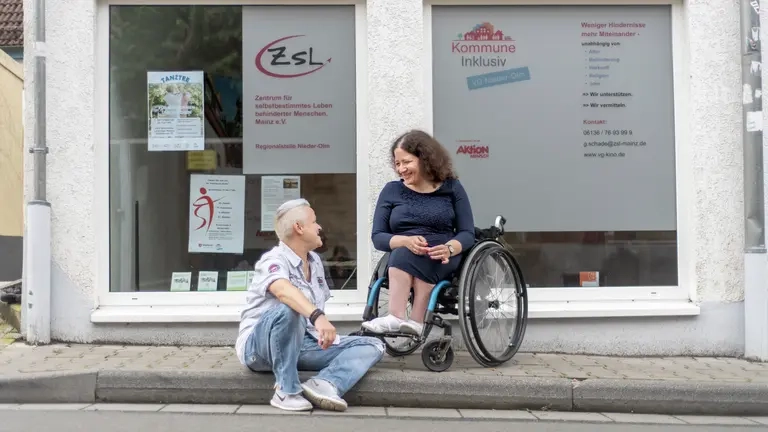 Zwei Frauen unterhalten sich von dem Kommune Inklusiv und ZSL Büro, eine sitzt im Rollstuhl.