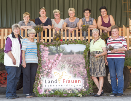 Mehrere Frauen stehen um ein großes Bild herum und lachen in die Kamera. Auf dem Bild ist Heidekraut zu sehen und der Schriftzug "LandFrauen Schneverdingen"