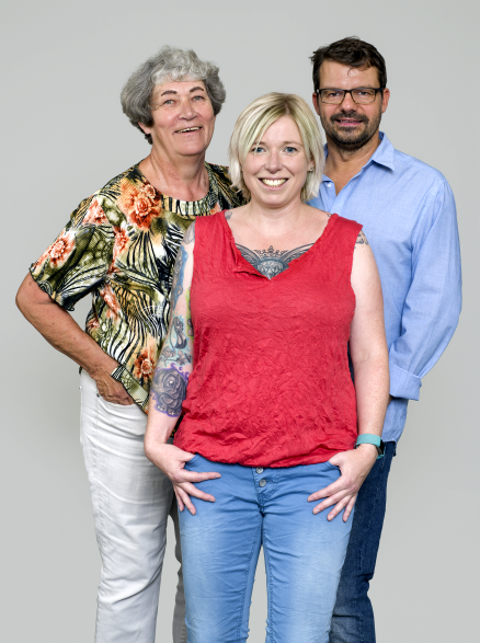 Zwei Frauen und ein Mann stehen zusammen und lachen in die Kamera.