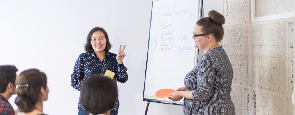 Zwei Frauen stehen vor einem Flipchart und halten einen Vortrag vor Publikum.