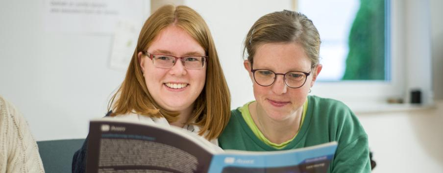 Zwei junge Frauen lesen gemeinsam in einer Broschüre