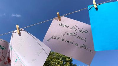 Ein Blatt Papier hängt an einer Schnur. Auf dem Zettel steht: "Wenn Vielfalt gelebt wird, fühle ich mich zu Hause."