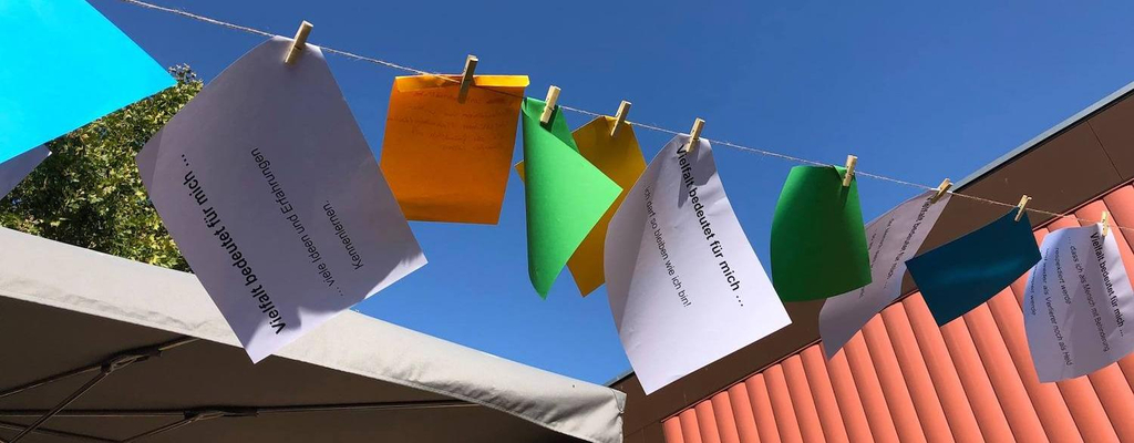 : Viele bunte Blätter Papier hängen an einer Leine. Auf jedem Blatt steht etwas.