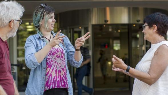 Zwei Frauen unterhalten sich in Gebärdensprache, ein Mann schaut zu