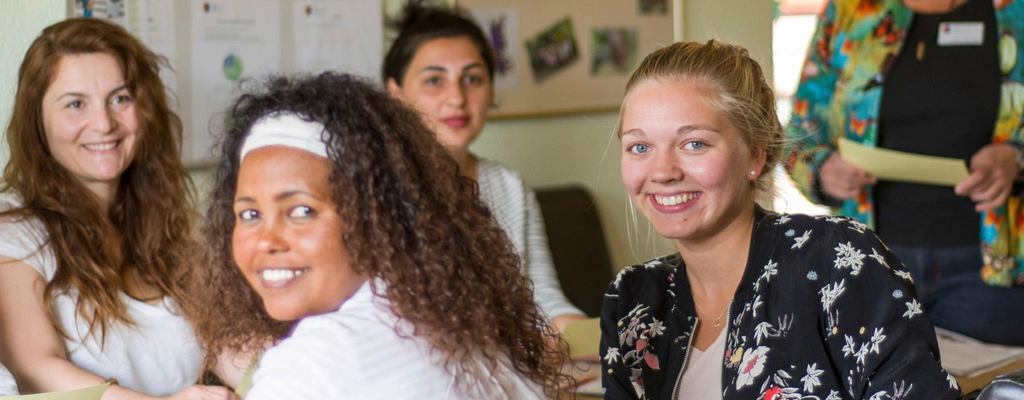 Eine Gruppe Frauen sitzt an einem langen Tisch. Zwei der Frauen haben sich zur Kamera gedreht und lächeln.