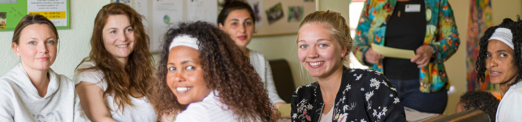 Eine Gruppe Frauen sitzt an einem langen Tisch. Zwei der Frauen haben sich zur Kamera gedreht und lächeln.
