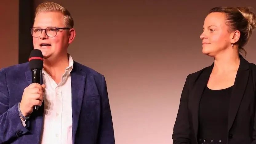 Erik Ortlieb und Anja Schulz stehen auf einer Bühne, Erik Ortlieb spricht in ein Mikrofon.