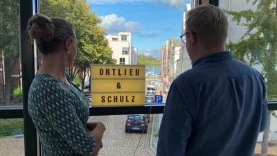 Eine Frau und ein Mann stehen mit dem Rücken zur Kamera und schauen aus dem Fenster.