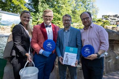 Das Kommune Inklusiv-Team aus Rostock zeigt im Rostocker Zoo die Urkunde über die Pinguin-Patenschaft.