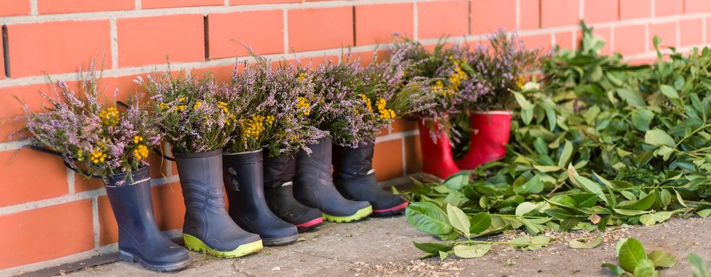 Eine Reihe von Gummistiefeln stehen vor einer Backsteinmauer. Sie sind gefüllt mit Heidekraut.