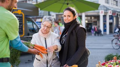 Eine Frau begutachtet die von einem Obstverkäufer präsentierten Möhren