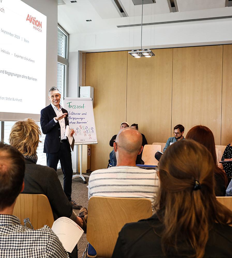 Ein Referent steht vor Publikum und hält einen Vortrag