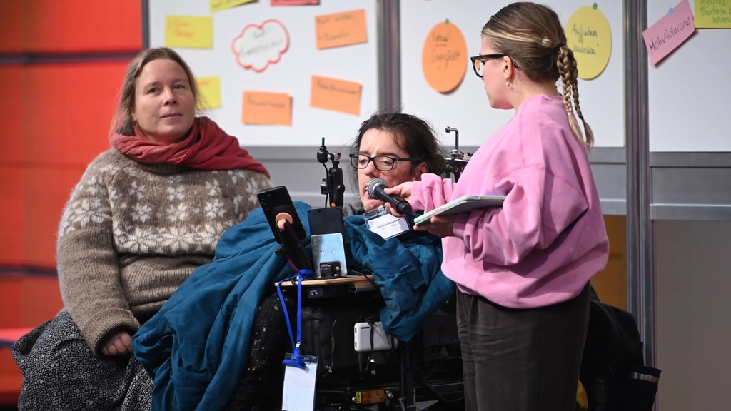 Ein Mann im E-Rolli wird von einer kleinwüchigen Frau interviewt.