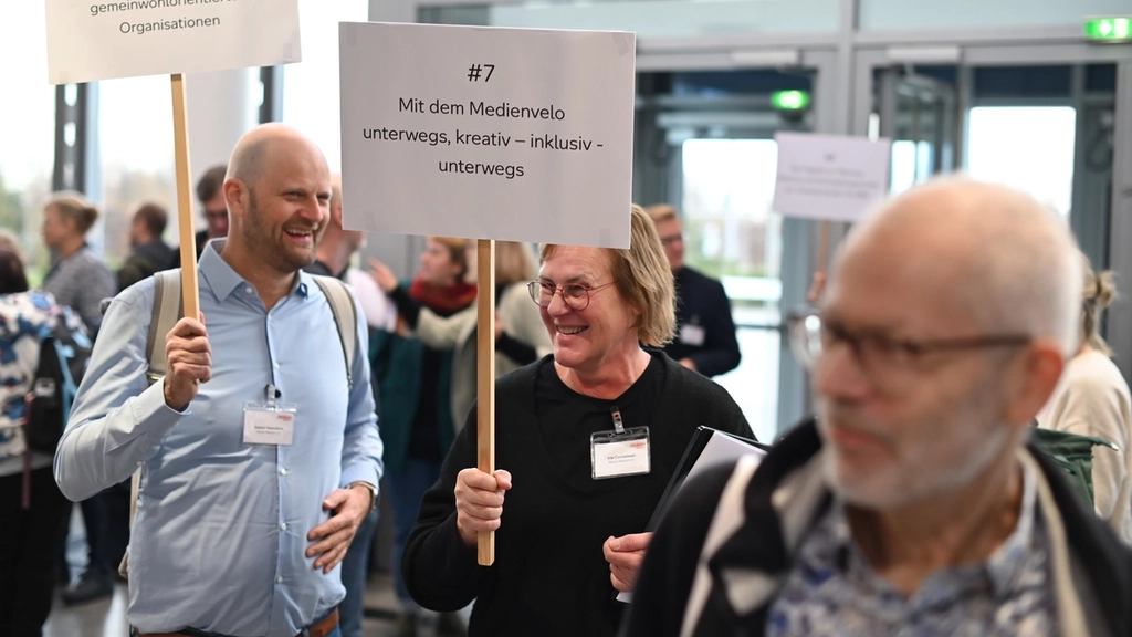 Zwei Personen halten beim Kongress Schilder mit dem Titel von Workshops in den Händen