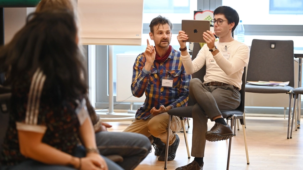 Workshopszene: Eine Person schaut auf ein Tablet, eine andere erklärt etwas.