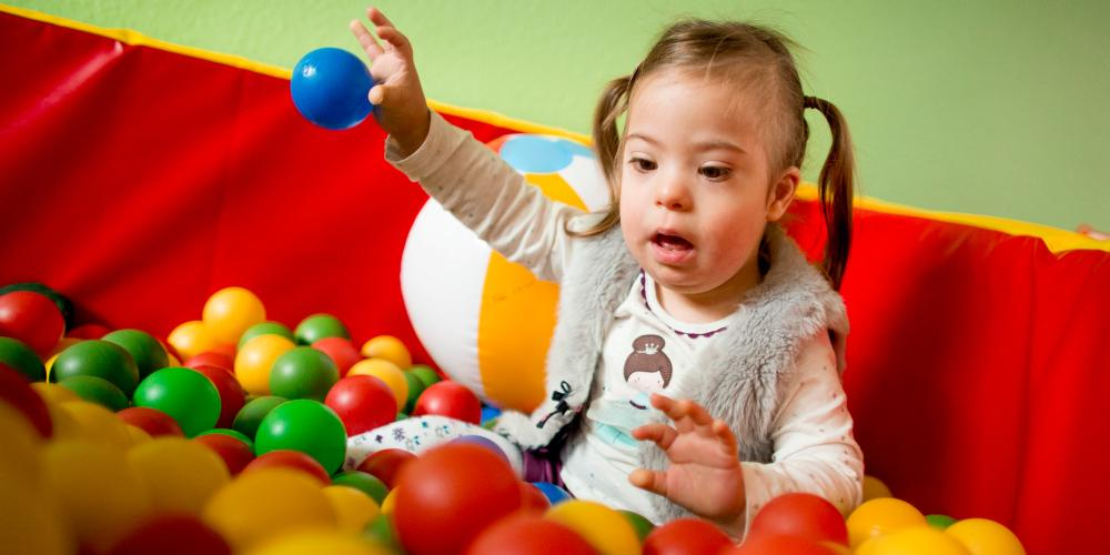 Ein kleines Mädchen mit Down-Syndrom spielt in einem Bällebad.