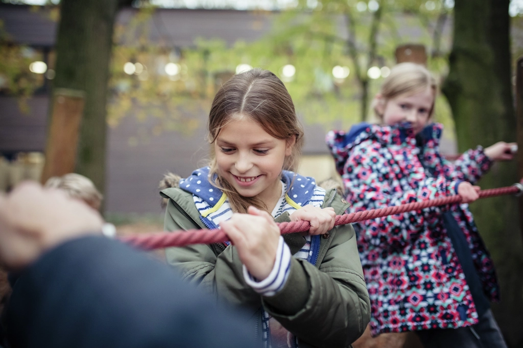 Zwei Mädchen balancieren und halten sich an einem dicken Seil fest. 