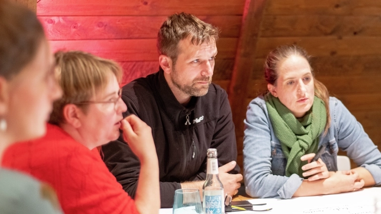 Vier Personen sitzen an einem Tisch und schauen konzentriert