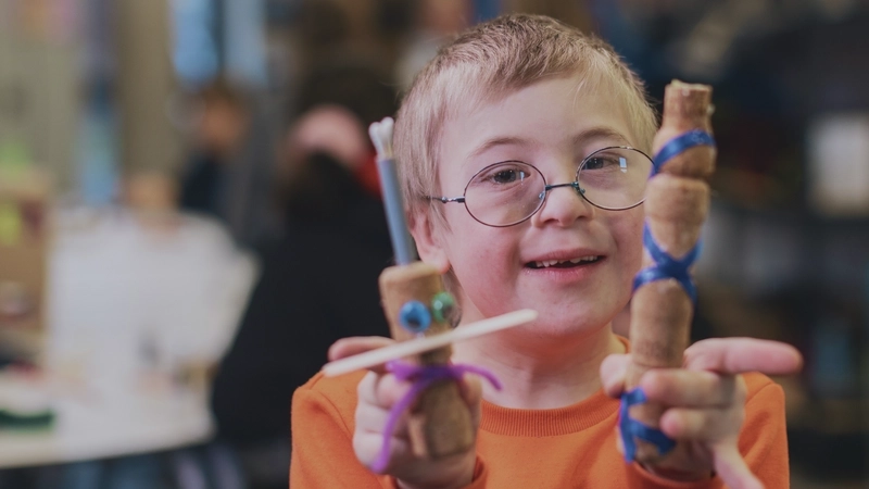 Ein Junge mit Downsyndrom zeigt zwei selbstgebastelete Figürchen