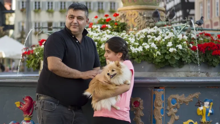Ein Mann und sein Kind stehen an einem Brunnen auf einem Platz.