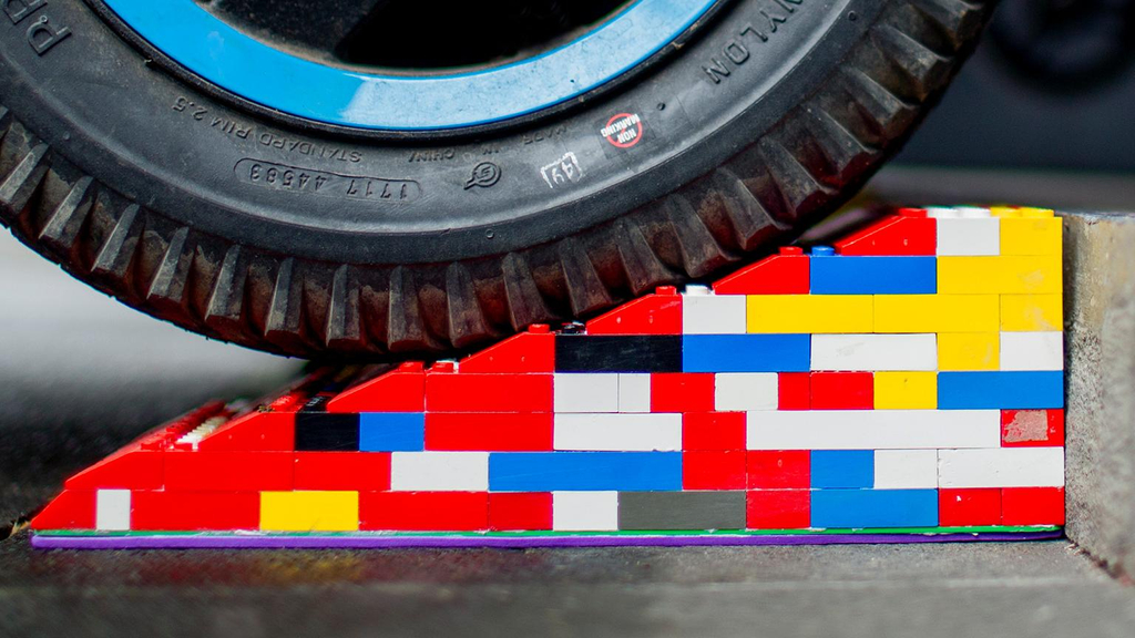 Eine bunte Legorampe liegt vor einer Stufe. Im Anschnitt ist ein Rollstuhl- oder Kinderwagen-Reifen zu sehen, der gerade über die Rampe rollt.