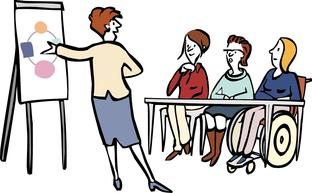 Drei Frauen, eine davon im Rollstuhl, sitzen an einem Tisch. Eine Frau steht vor einer Tafel und erklärt eine Zeichnung.