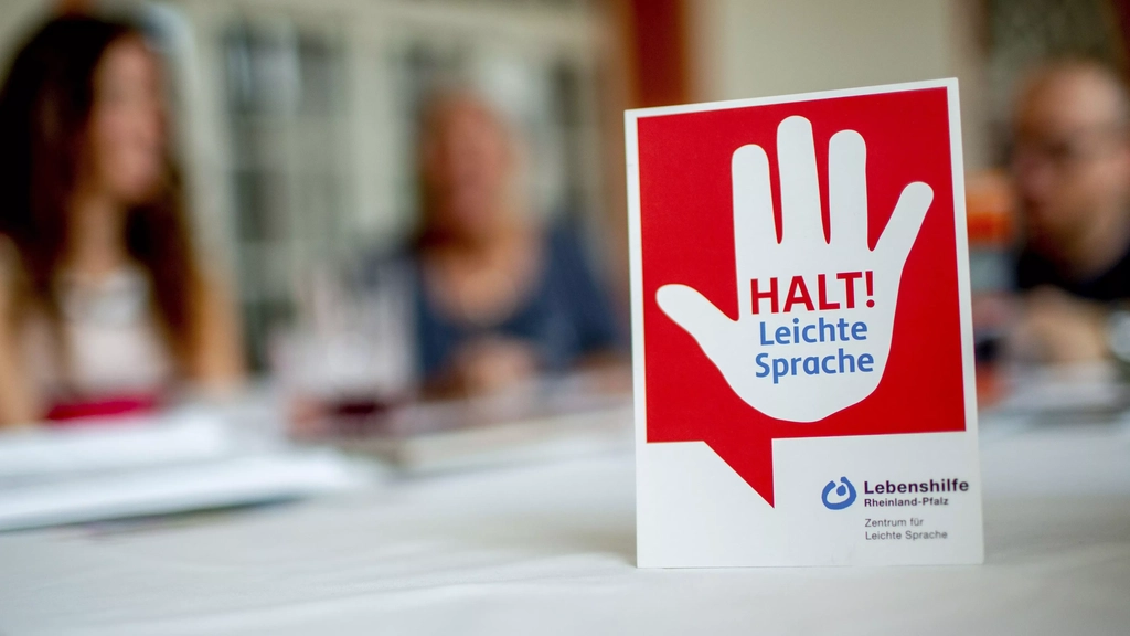 Auf einem Tisch steht ein Schild mit einer warnenden Hand und dem Hinweis: Halt! Leichte Sprache!