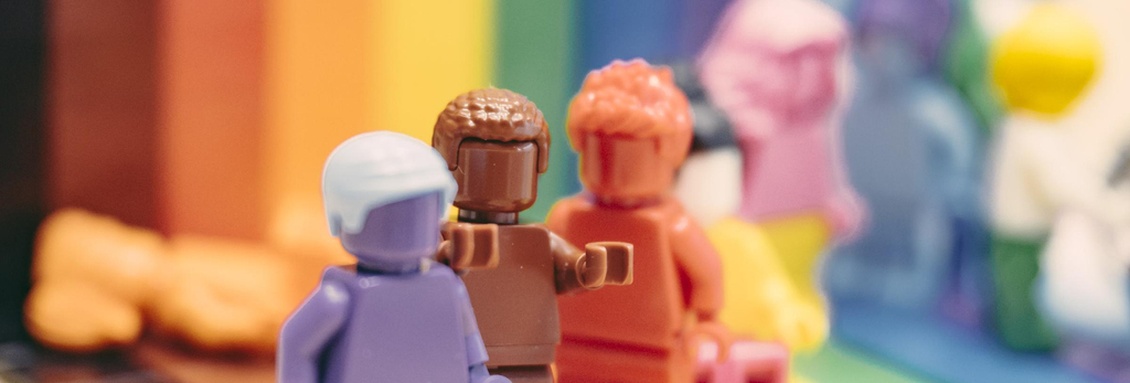 Mehrere bunte Legofiguren vor einem regenbogenfarbenen Hintergrund