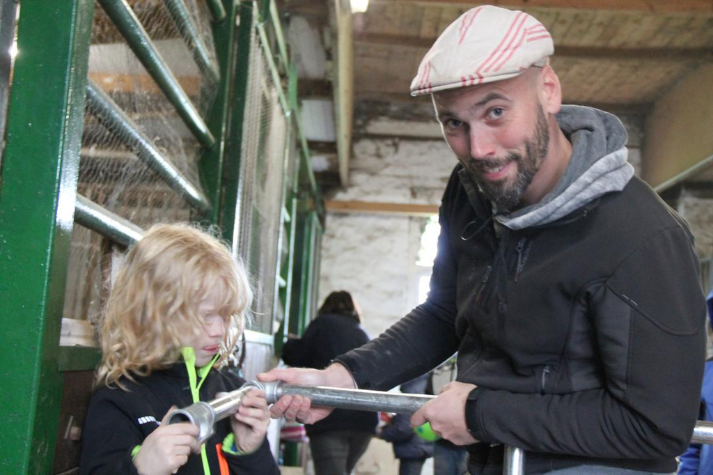 Ein Mann und ein kleines Mädchen halten ein Rohr in den Händen und stehen in einem Stall.