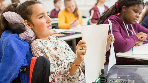 Eine Schülerin im Rollstuhl in einem gefüllten Klassenzimmer.
