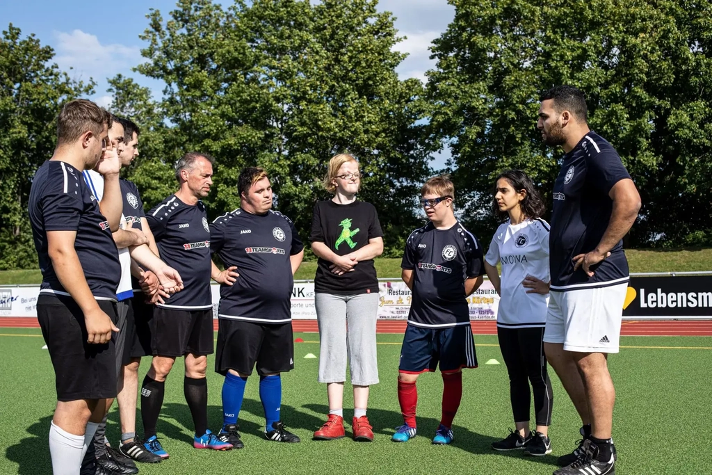 Trainer Gökhan erklärt einer Gruppe von Fußballspieler*innen etwas und alle schauen ihn interessiert an.