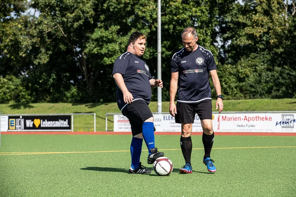 Zwei Mitglieder des FC Germania Zündorf, Daniel und Frank, stehen auf dem Fußballplatz und trainieren mit dem Ball.