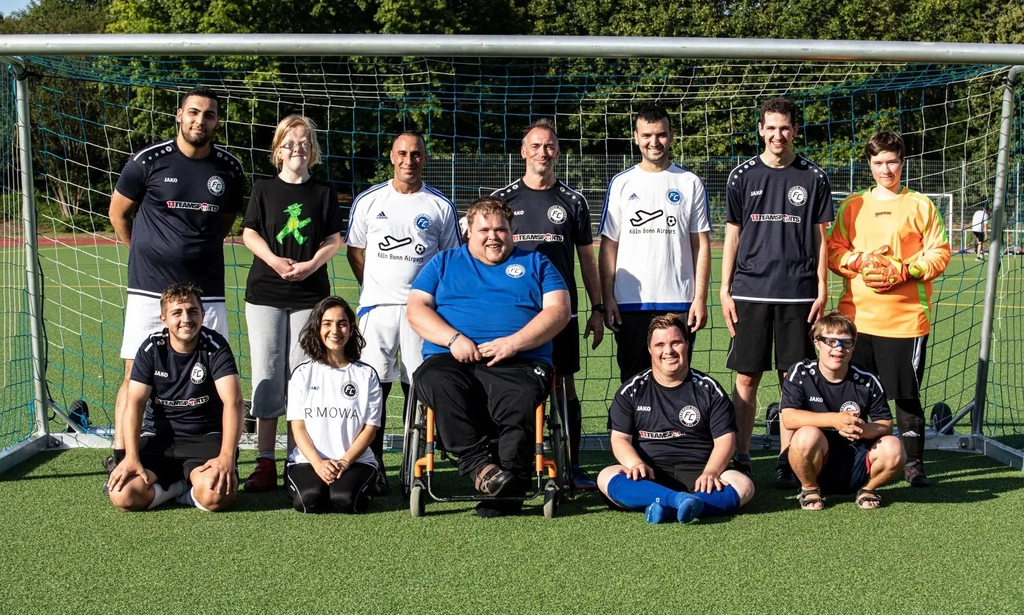 Spieler*innen des FC Germania Zündorf posieren mit dem Trainer*innenteam vor einem Fußballtor.