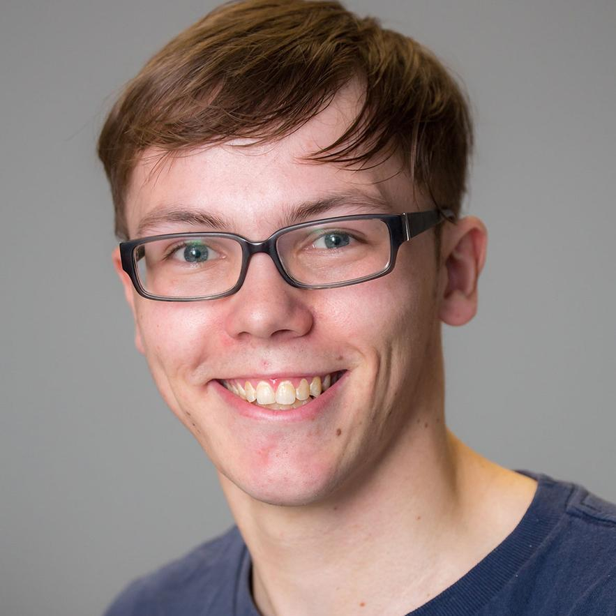 Porträt eines jungen freundlich lächelnden Mannes mit braunen kurzen Haaren und Brille.