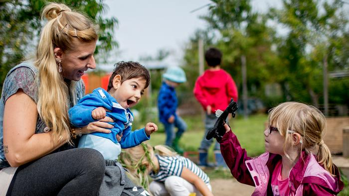 Frau unterstützt einen Jungen mit Behinderung, der mit einem Mädchen spielt.